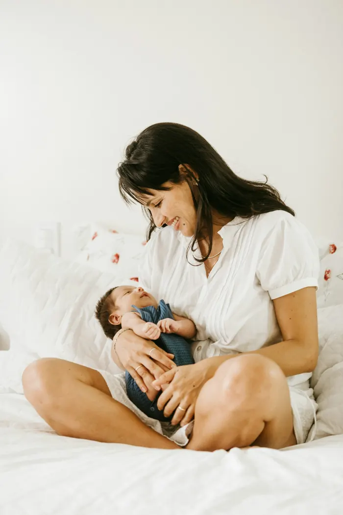 Une maman assise sur son lit, son bébé dans les bras